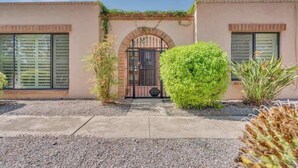 A building with a gated entrance, a small garden area with shrubs, and a paved walkway. - Warm & Quaint Retreat with Pool (Tucson)