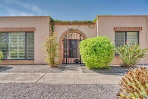 A building with a gated entrance, a small garden area with shrubs, and a paved walkway. - Warm & Quaint Retreat with Pool (Tucson)