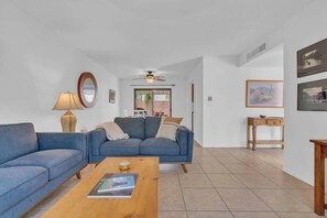 Un salon comprenant un canapé, une table basse, une lampe, un ventilateur de plafond et des œuvres d’art accrochées aux murs.