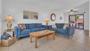 A living room with a blue sofa, two lamps, a wooden coffee table, and a ceiling fan. - Warm & Quaint Retreat with Pool (Tucson)