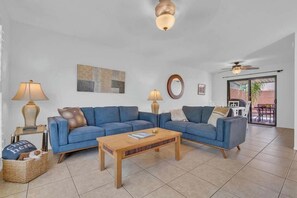 A living room with a blue sofa, two lamps, a wooden coffee table, and a ceiling fan. - Warm & Quaint Retreat with Pool (Tucson)
