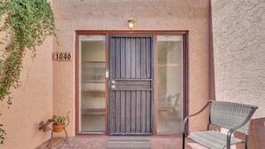 A building entrance with a number '1046' on the wall, a metal gate, a potted plant, and a wicker chair. - Warm & Quaint Retreat with Pool (Tucson)