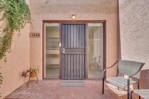 A building entrance with a number '1046' on the wall, a metal gate, a potted plant, and a wicker chair. - Warm & Quaint Retreat with Pool (Tucson)