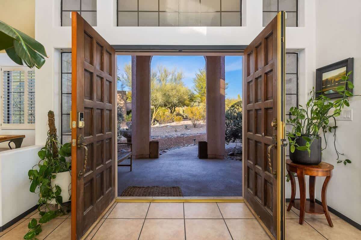 Entrada de hotel com uma grande porta de madeira, um vaso de planta e vista para a área externa.