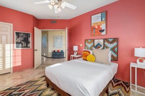 Ein Schlafzimmer mit einem Bett, Deckenventilator, einer Tür und einer Wand mit Kunstwerken.