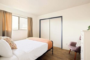 A bedroom with a bed, a wardrobe, a chair, and a window with curtains. - Midtown Retreat-Pet Friendly (Tucson)