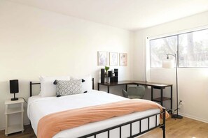 A bedroom with a bed, bedside table, desk, chair, and a window with a view. - Midtown Retreat-Pet Friendly (Tucson)