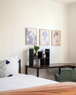 Ein Hotelzimmer mit einem Bett, einem Schreibtisch und zwei gerahmten Kunstwerken an der Wand.