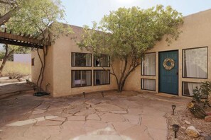 A building with a stone patio, a blue door with a wreath, and windows with curtains. - Midtown Retreat-Pet Friendly (Tucson)