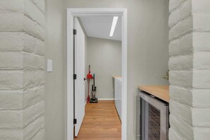Un corridoio stretto con pareti in mattoni bianchi, pavimento in legno e una zona cucina visibile in fondo.