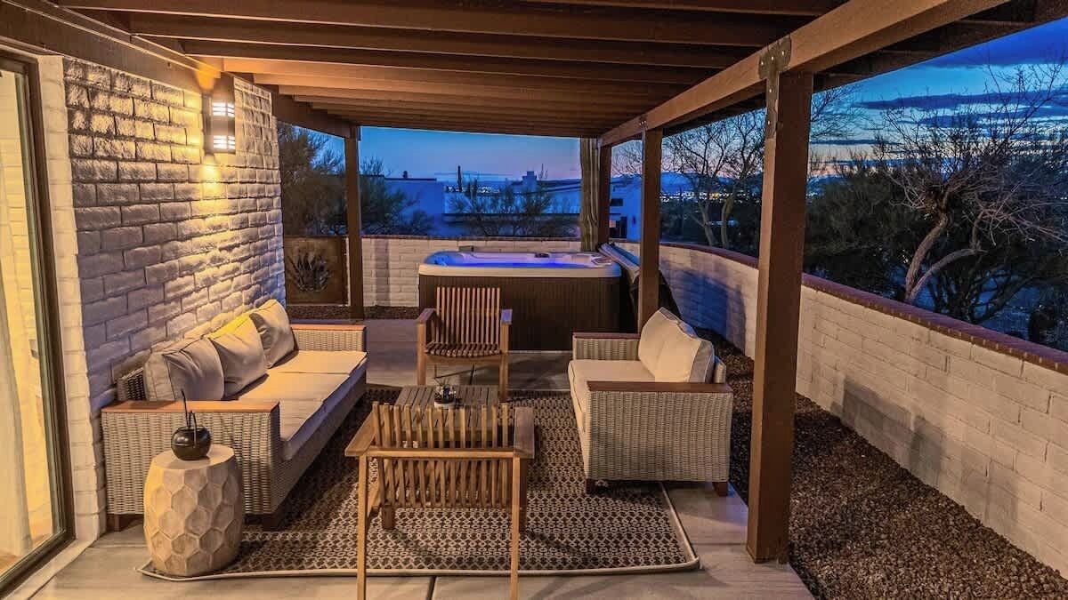 A covered outdoor seating area with a hot tub, wicker furniture, and a view of the cityscape at dusk.