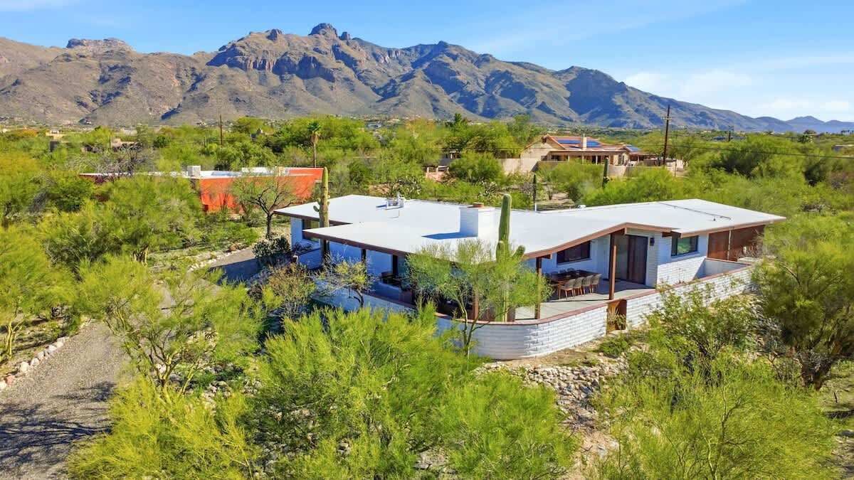 Una casa moderna con techo plano, rodeada de vegetación y montañas al fondo.