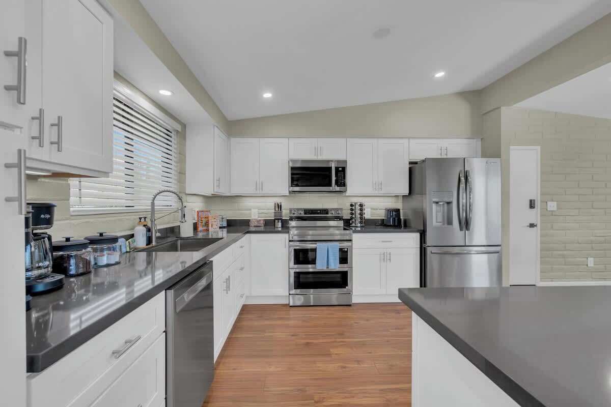 A modern kitchen with white cabinets, stainless steel appliances, and a wooden floor.