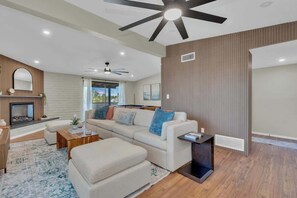 Ein modernes Wohnzimmer mit Kamin, Deckenventilator und großem Fenster.
