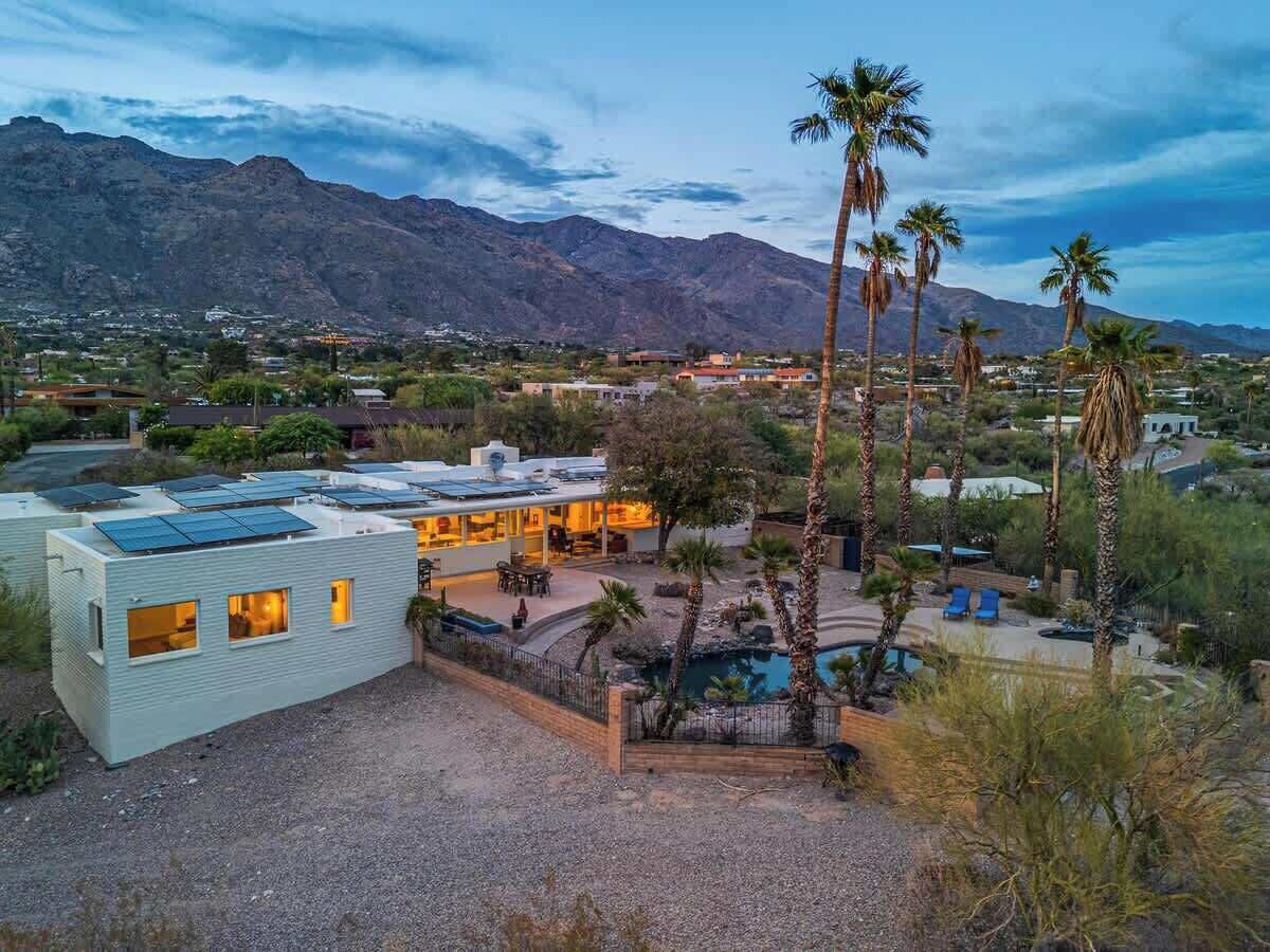 A residential area with a house featuring solar panels, a swimming pool, and a mountainous backdrop.