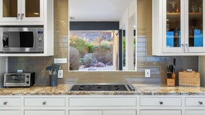 A kitchen with a built-in microwave, a toaster, a window with a view of a garden, and cabinets with glass doors. - Cactus & Sky Escape with POOL and SPA! (Tucson)
