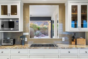 Eine Küche mit integriertem Mikrowellenherd, einem Toaster, einem Fenster mit Gartenblick und Schränken mit Glastüren.