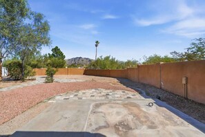Un pati amb una zona pavimentada, camins de grava i una paret.
