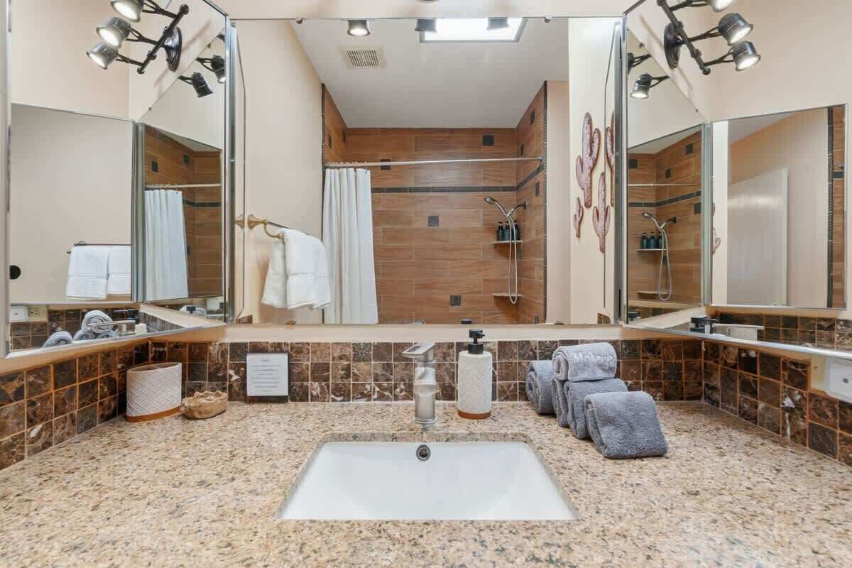 Une salle de bain avec un grand miroir, un lavabo, une douche et un porte-serviettes.