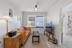 A compact living space with a sofa, a small table, a lamp, a radiator, a window with patterned curtains, and a ceiling fan. - Santa Rosa Hideaway near TCC (Tucson)