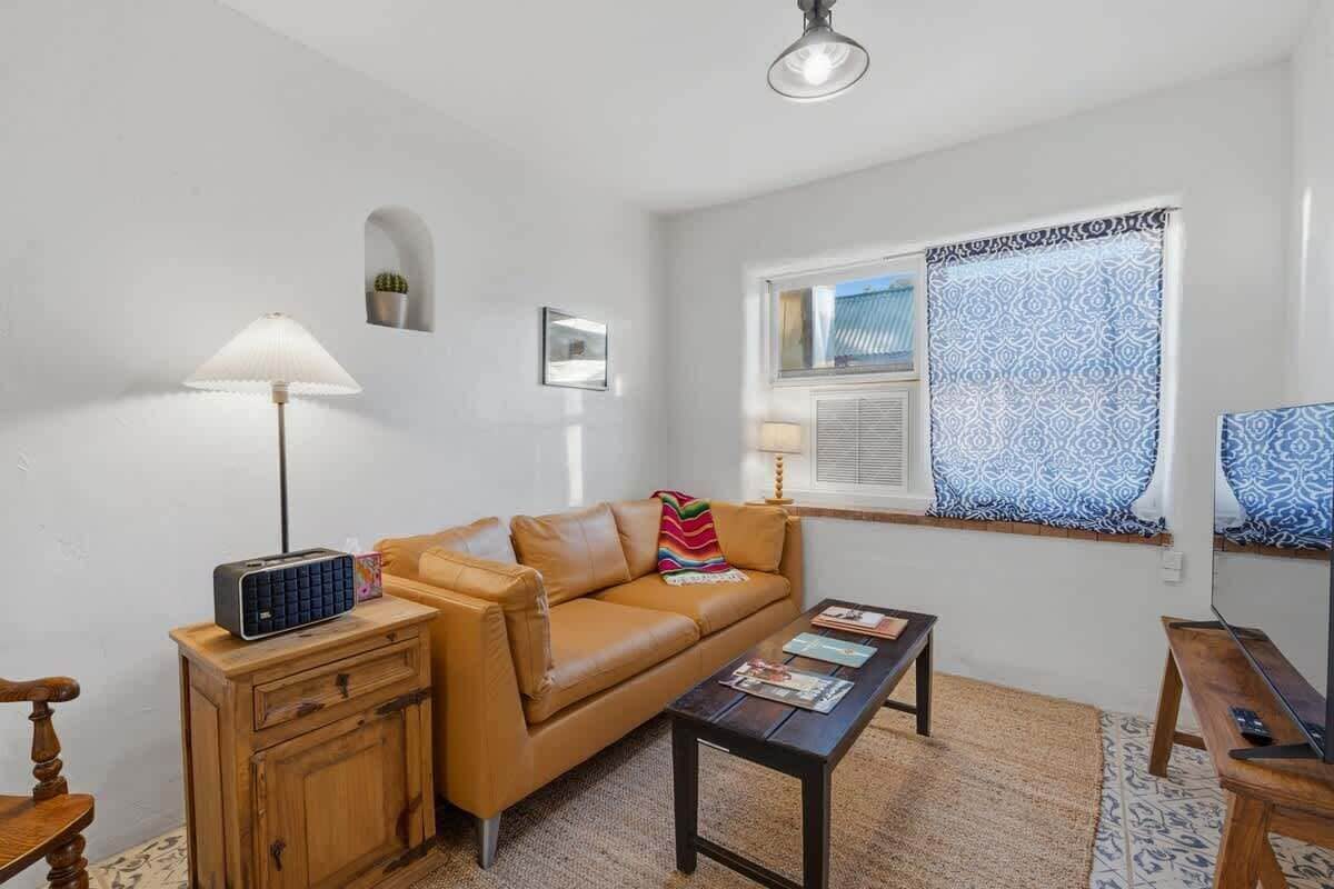 A living room with a sofa, a coffee table, a lamp, a radio, a TV, and a window with patterned curtains.