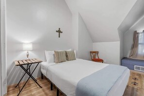 A bedroom with a bed, a small table, a chair, a cross on the wall, and a window with curtains. - Santa Rosa Hideaway near TCC (Tucson)