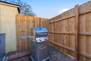 A portable stainless steel barbecue grill with a lid and two burners, positioned in a backyard with a wooden fence. - Santa Rosa Hideaway near TCC (Tucson)