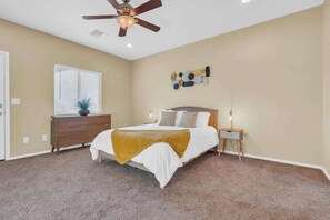 Ein Schlafzimmer mit Bett, Schminktisch, Nachttisch, Deckenventilator und Wanddekoration.
