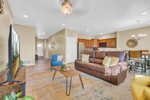 A spacious living room with a brown leather sofa, a blue armchair, a wooden coffee table, and a flat-screen TV. - Desert Escape- 5 Mins to Starr Pass & Hiking (Tucson)