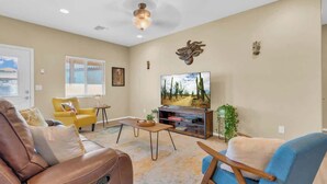 Un salon comprenant un canapé, des fauteuils, une table basse, un téléviseur et une fenêtre avec des stores.