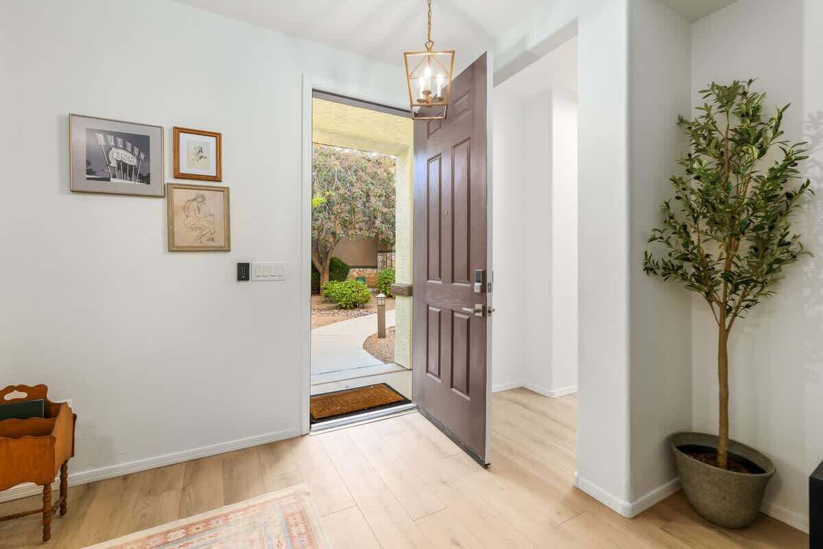 A hallway with a wooden floor, a dark wooden door, a potted plant, and framed artwork on the wall.