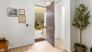 Ein Korridor mit Holzboden, einer dunklen Holztür, einem Blumentopf und gerahmten Bildern an der Wand.