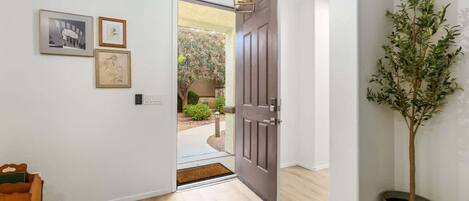 A hallway with a wooden floor, a dark wooden door, a potted plant, and framed artwork on the wall.