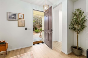 A hallway with a wooden floor, a dark wooden door, a potted plant, and framed artwork on the wall. - Peaceful 2 Story Home-Pet Friendly (Tucson)