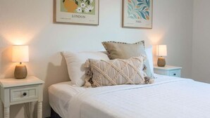 Ein ordentlich bezogenes Bett mit weißer Daunendecke, zwei Kissen und einem Nachttisch mit Lampe.