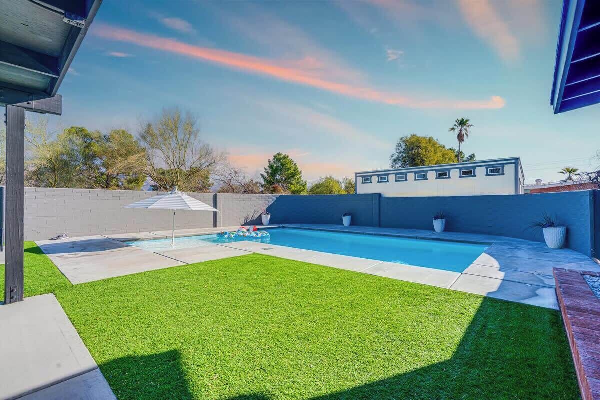A swimming pool with artificial grass, a patio area, and a building in the background.