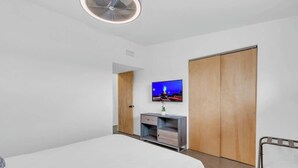 A bedroom with a bed, a TV, a wooden wardrobe, and a small desk with drawers. - Mid-Century Desert Galore/Mt.Views/Pool (Tucson)