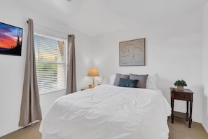 A bedroom with a bed, a nightstand, a lamp, a window with curtains, and a wall-mounted painting. - Family Home-mins from the LOOP with Hot Tub! (Tucson)