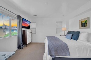 A bedroom with a bed, a TV, a dresser, a window with curtains, a lamp, and a painting on the wall. - Family Home-mins from the LOOP with Hot Tub! (Tucson)