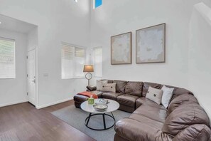 A modern living room with a brown leather sofa, a round coffee table, and two abstract paintings on the wall. - Family Home-mins from the LOOP with Hot Tub! (Tucson)