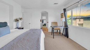 Ett hotellrum med en säng, en stol, ett bord, ett fönster med utsikt och en dörr som leder till ett annat rum.