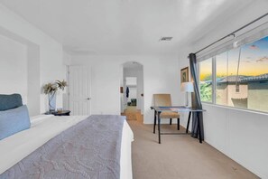 Ein Hotelzimmer mit einem Bett, einem Sessel, einem Tisch, einem Fenster mit Blick und einer Tür zu einem anderen Raum.
