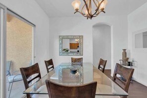Un comedor con mesa de vidrio, sillas de madera, una araña y un espejo decorativo.