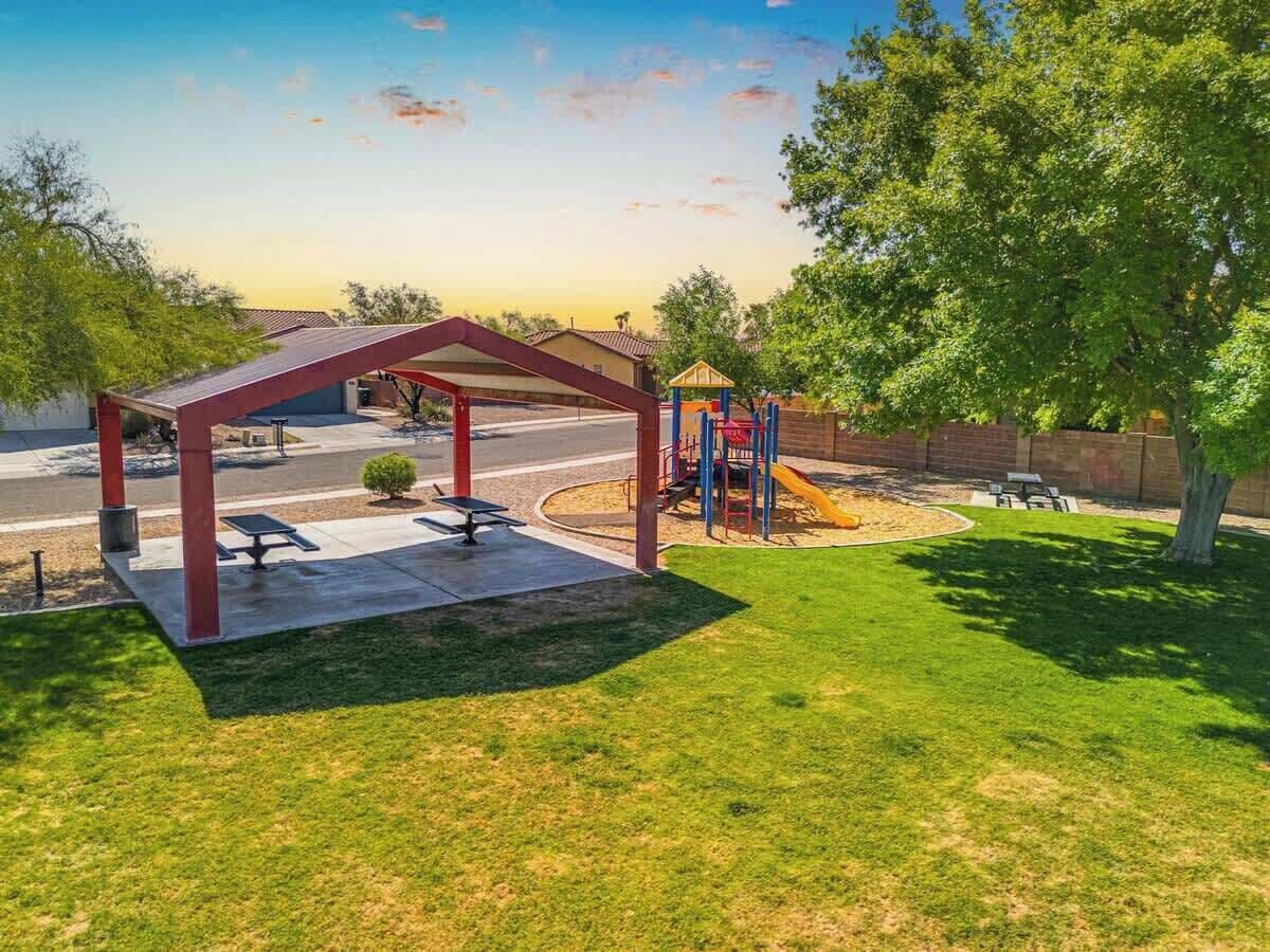 Ein überdachter Außenbereich mit Spielplatz, Picknicktischen und einem gepflegten Rasen.