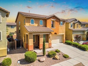 A residential building with a tiled roof, a garage, and a well-maintained front yard with shrubs and a small tree. - Family Home-mins from the LOOP with Hot Tub! (Tucson)