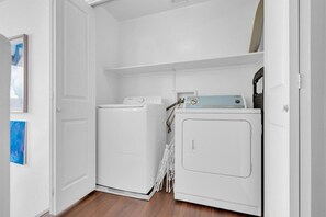 Ein Waschraum mit Waschmaschine und Trockner, einer Tür und einem an der Wand befestigten Wäscheständer.
