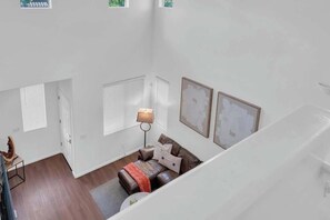 Um quarto com pé direito alto, um sofá de couro marrom, uma luminária e quadros nas paredes.