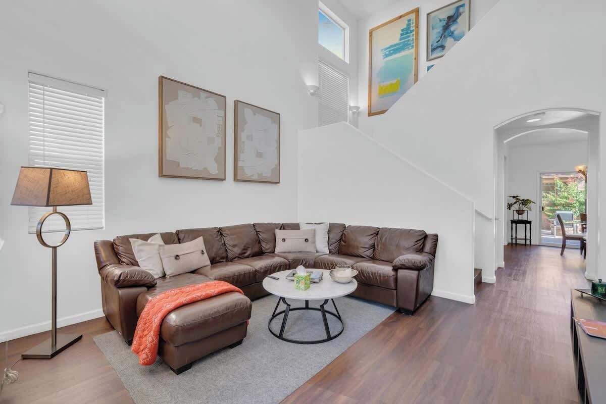 Una sala moderna con un sofá seccional de cuero marrón, una mesa de centro redonda y una lámpara de pie. Hay una escalera que conduce a un nivel superior.
