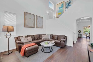 Ein modernes Wohnzimmer mit einem braunen Ledersofa, einem runden Couchtisch und einer Stehlampe. Eine Treppe führt zu einer oberen Ebene.