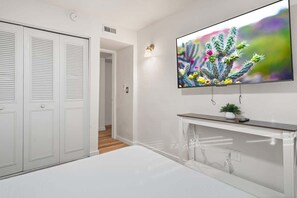 Ein modernes Zimmer mit einem weißen Schrank, einem an der Wand befestigten Fernseher und einer kleinen Pflanze auf einem Beistelltisch.